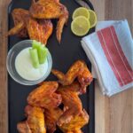 Ume plum chicken wings on a cast iron platter with celery, yogurt dipping sauce, and lemon slices